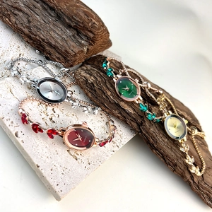 Close-up of luxury oval quartz watches with metallic leaf-style bands on stone display