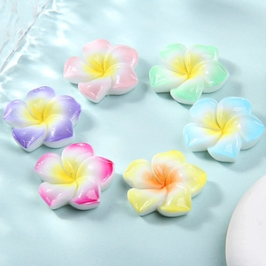 Macro detail of six gradient resin frangipani charms floating on clear blue water