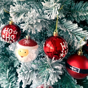 Detailed view of red and clear Christmas balls with HO HO HO text on snowy pine tree