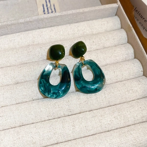 Macro detail of geometric resin earrings with marble texture and teal green teardrops