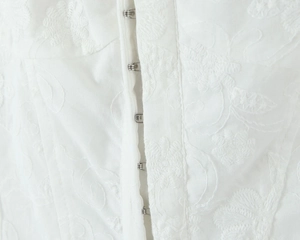 Detailed view of white floral embroidery with vertical metal hook-and-eye closures