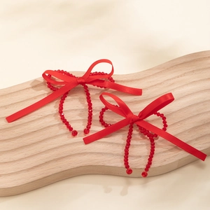 Detail of red ribbon bow earrings with faceted crystal beads on a wooden display