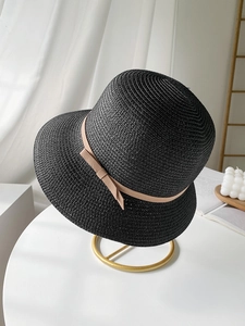 Detail of a black straw sun hat featuring a beige ribbon bow on an elegant metal stand
