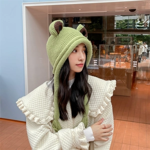 Detail der grünen Frosch-Strickmütze mit langen geflochtenen Ohrenklappen am Modell