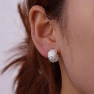 Close-up of silver C-shape earring with frosted texture shown on a female ear