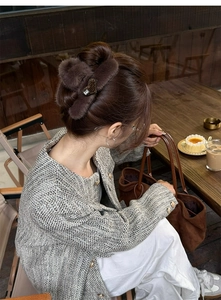 Detail of dark brown plush hair claw with leopard heart on model in a cozy cafe setting