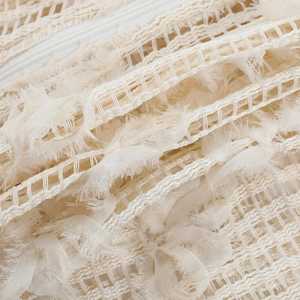 Dettaglio macro del pizzo color crema con frange decorative e cerniera bianca invisibile