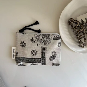 Close-up of grey paisley canvas pouch featuring tassel zipper and simple wish label