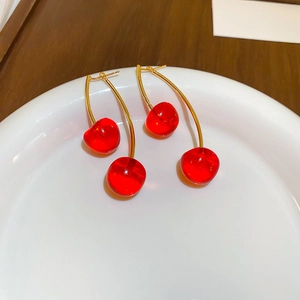 Macro view of sweet red resin cherry earrings with golden hooks on white ceramic plate