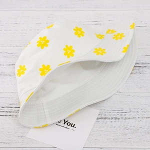 Flat lay of white cotton bucket hat with vibrant yellow floral patterns on wood surface