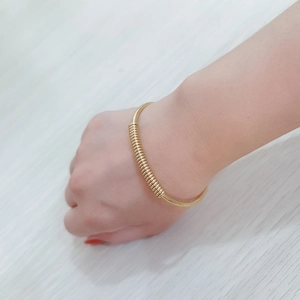 Close-up of gold stainless steel spring bracelet worn on wrist against a wood background
