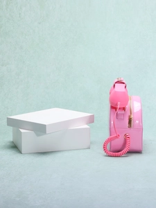 Pink telephone-shaped shoulder bag in glossy patent leather shown from a side view