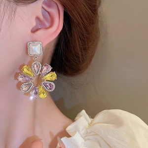 Détail de boucles d'oreilles fleurs avec pierres jaunes et violettes et perle carrée