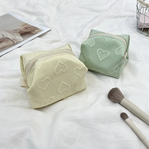 Détail de trousses à maquillage crème et vertes avec motif cœur gaufré et dragonne latérale