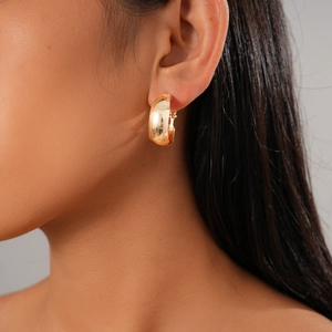 Close-up of model wearing wide gold-finish C-shaped hoop earrings with a mirror-like surface