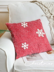 Detail of red plush Christmas pillow with white snowflake patterns on a sofa