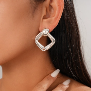 Close-up of polished silver geometric square stud earrings worn on a female model