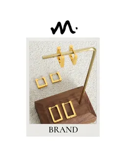 Detailed view of three sizes of geometric rectangular gold earrings on a wooden stand