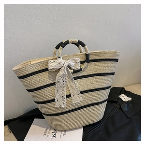 Detailed close-up of straw tote bag with black stripes and white lace bow decoration