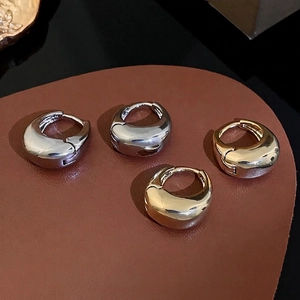 Minimalist thick hoop earrings in polished gold and silver finishes on leather display