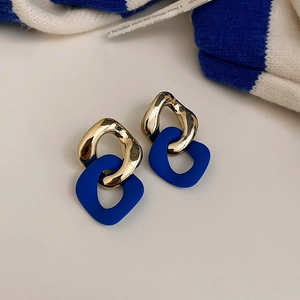 Detail of geometric gold and Klein blue interlocking earrings on white background