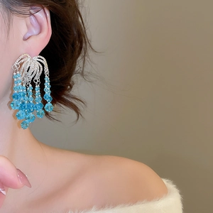 Detail view of long tiered fringe earrings with blue crystal beads on a female model