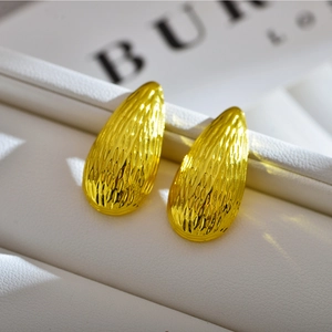 Macro shot of gold teardrop earrings with textured hammered finish on a white stand