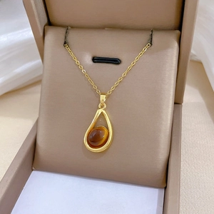 Detail of a gold waterdrop pendant necklace with amber stone on a velvet display