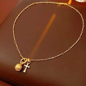 Dettaglio macro del ciondolo a croce dorata e sfera filigranata su collana di lusso