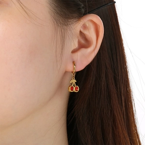 Detailed view of gold cherry earrings with red stones on a model, elegant fruit jewelry style