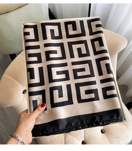 Detail of a chic houndstooth silk scarf in beige and black folded on a velvet chair