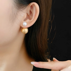 Detail of elegant gold metal and silver pearl drop earrings worn by a model