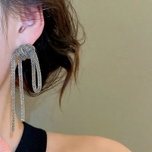 Close-up of silver mesh knot tassel earrings worn by a model in a trendy retro style