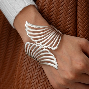 Close-up of silver hollow wing cuff bracelet on wrist featuring a metallic feather design