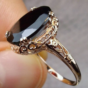 Macro detail of vintage rose gold ring with red zircon stone and intricate hollow floral carvings
