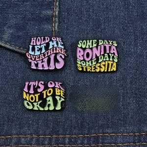 Detail of four colorful enamel lapel pins with witty quotes on blue denim fabric