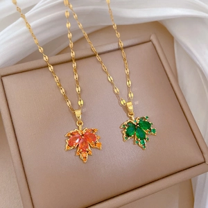 Macro detail of gold maple leaf pendants with orange and green zircon stones on silk