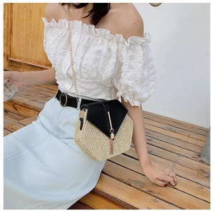 Detail of woven crossbody bag with black flap, gold tassel, and metal chain strap