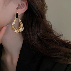 Golden geometric earrings with black gemstone and pleated metal design on a model