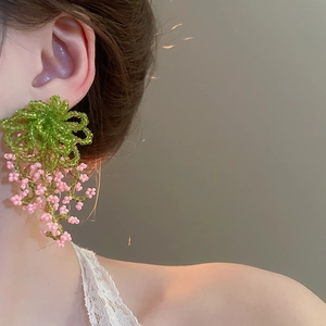 Detailed close-up of handmade green and pink beaded floral tassel earrings worn on a model