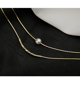 Detail view of gold double-layer necklace with baroque pearl on black leather background