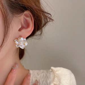 Close-up of model wearing white flower earring with gold trim and central pearl detail