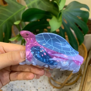 Detail of a sea turtle shaped acrylic hair claw clip with pink and blue gradient finish