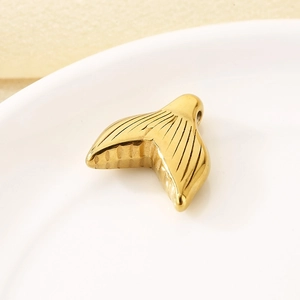 Macro detail of 18k gold plated stainless steel fishtail pendant on a white ceramic plate