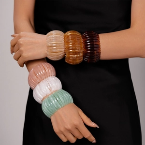 Détail de larges bracelets en résine nervurée de plusieurs couleurs portés par un mannequin