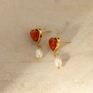 Close-up of 18k gold earrings with red heart stones and white pearl pendants on marble