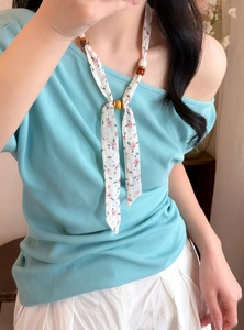 Close-up detail showing a floral printed chiffon necklace with wooden beads on a model