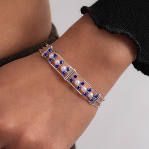 Nahaufnahme eines dreilagigen silbernen Armreifs mit blauen Kristallen und Perlen.