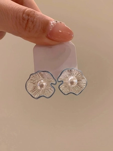 Detailed close-up of a silver flower earring with blue petals and a central white pearl
