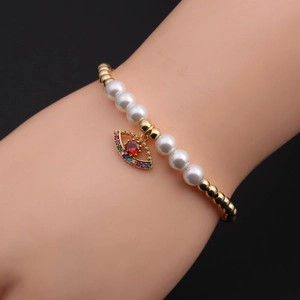 Detailed macro view of the evil eye pendant on a gold and pearl bracelet for women